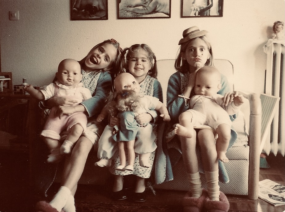 Three young sisters in vintage outfits holding dolls — Andrea with her sisters.